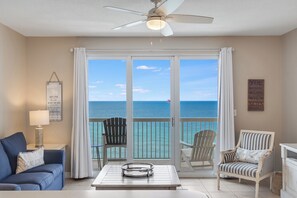 A room with a view of the ocean, a ceiling fan, a table with a tray, a blue sofa, and striped chairs.