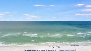 A beach with clear blue water, a sandy shore, and several blue umbrellas lined up.