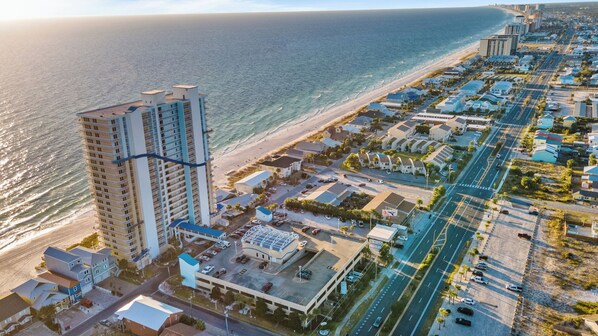 A coastal hotel with multiple floors, a parking lot, and a beach view.