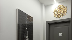 A hallway with a framed picture of a building, a dark door with a number plaque, and a decorative gold leaf wall piece. - Dorolea Rooms Torino Centro (Turin)