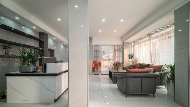 Una cocina moderna con encimera de mármol y una isla central, un área de estar con un sofá gris y una mesa de centro, y un amplio ventanal con cortinas de gasa.