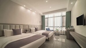 Habitación de hotel moderna con dos camas, televisión, una mesita y ventana con cortinas.