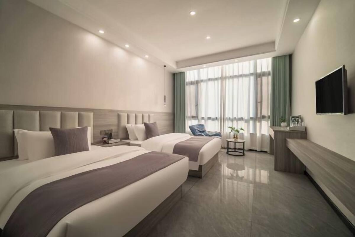 A modern hotel room with two beds, a TV, a small table, and a window with curtains.