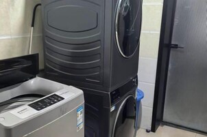 Un lavadero compacto y moderno con lavadora y secadora de carga frontal, un pequeño contenedor de basura y una puerta que da a otra habitación.