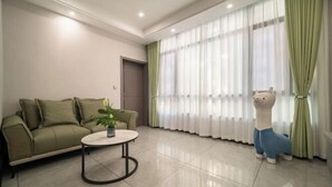 Una sala de estar con un sofá, una mesa redonda de centro, una planta en maceta y un ventanal con cortinas traslúcidas.