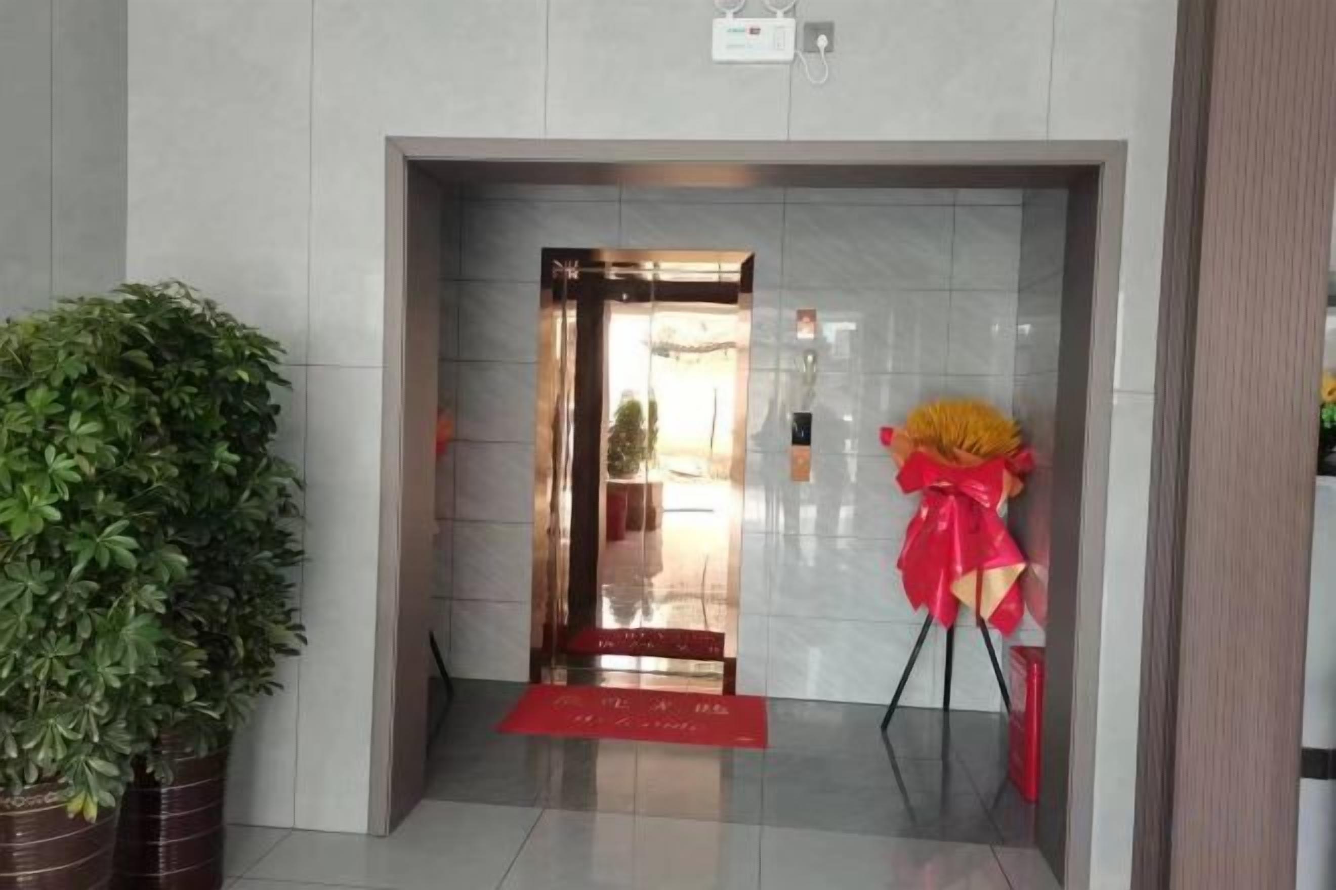 An entrance with a red mat, a potted plant, and a red and yellow floral arrangement.
