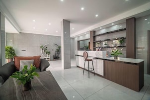 Cozinha moderna com área de bar, mesa de jantar com cadeiras e sala de estar com sofá e planta.