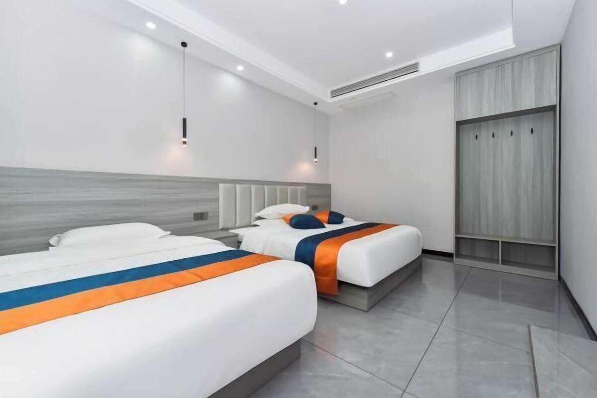 A modern hotel room with two beds, a wardrobe, and a large window.