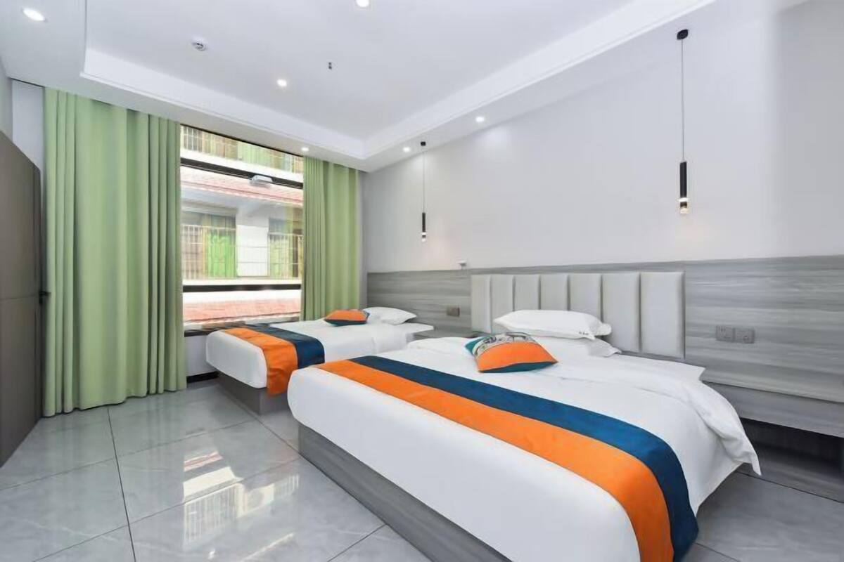 A hotel room with two beds, a large window with curtains, a modern light fixture, and a view of a building outside.