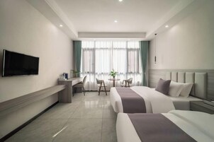 Una habitación de hotel con cama, escritorio, silla, televisor y ventana con cortinas.