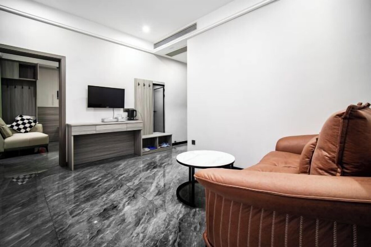 A modern hotel room with a sofa, a small round table, a TV mounted on the wall, and a minibar.