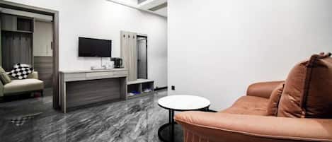 Una habitación de hotel moderna con un sofá, una mesita redonda, un televisor montado en la pared y un minibar.