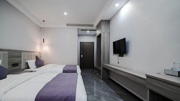 A hotel room with two beds, a flat-screen TV mounted on the wall, a desk with a computer, and a modern design. - Huangguoshu Guchunxiang Homestay (Zhenning)