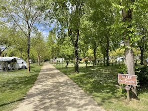 Un terrain de camping avec un chemin de terre, des tentes et un panneau indiquant « Allée des Saules ».