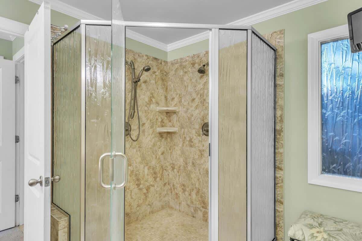 A glass-enclosed shower with a marble wall, a bench, and a window with a bamboo pattern view.