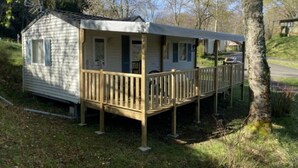 A small, single-story mobile home with a porch and a fenced deck. - ZEcamping 4 étoiles familial piscine couverte locatif TV 31m2 (Vic-sur-Cère)