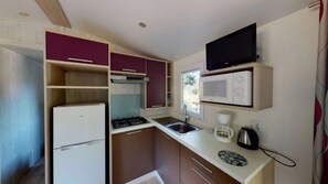 A compact kitchen with a refrigerator, stove, microwave, and a coffee maker. - ZEcamping 4 étoiles familial piscine couverte locatif TV 31m2 (Vic-sur-Cère)