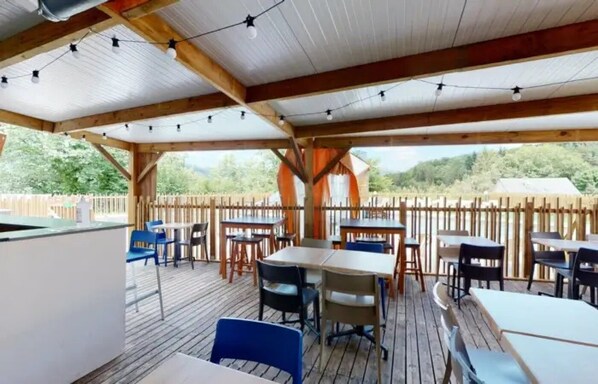 An outdoor patio area with wooden tables and chairs, a white counter, and string lights.