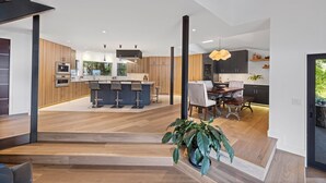 Eine moderne Küche mit Holzausstattung, einer zentralen Kochinsel mit Barhocker und einem Essbereich mit Tisch und Stühlen.