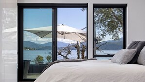 Ein Schlafzimmer mit einem großen Bett, einer Schiebetür zu einem Balkon mit Blick auf einen See und Berge.