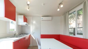 Cocina compacta con encimera blanca, armarios rojos y una mesa de comedor blanca con sillas.