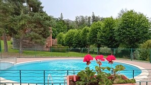 A swimming pool surrounded by a green fence, with a brick wall and trees in the background. - ZEcamping 3* locatif TV 34m2 2 pers (Vorey)