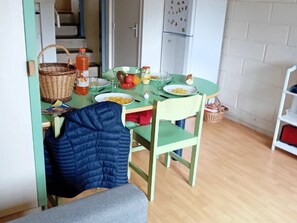 Zona pranzo con tavolo apparecchiato per due, un cesto di vimini, una bottiglia di salsa e una ciotola di cibo.