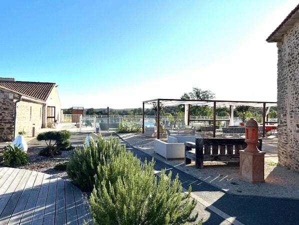 A rooftop patio with outdoor seating, a stone building, and a view of a body of water.