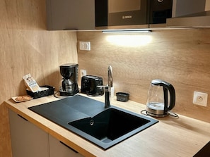 A modern kitchen with a black sink, a coffee maker, and a toaster. - ZEcamping 3 étoiles piscine cottage TV LV 42m2 6 pers (Vouvant)