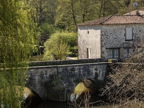 A stone bridge over a body of water, with a building featuring a stone facade and a tiled roof in the background. - ZEcamping 3 étoiles piscine cottage TV LV 42m2 6 pers (Vouvant)