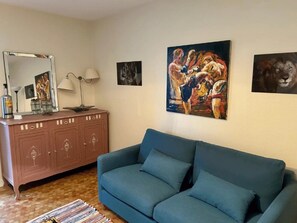A living room with a blue sofa, a wooden cabinet, and three framed artworks on the wall. - ZEcamping 3 étoiles piscine cottage TV LV 42m2 6 pers (Vouvant)