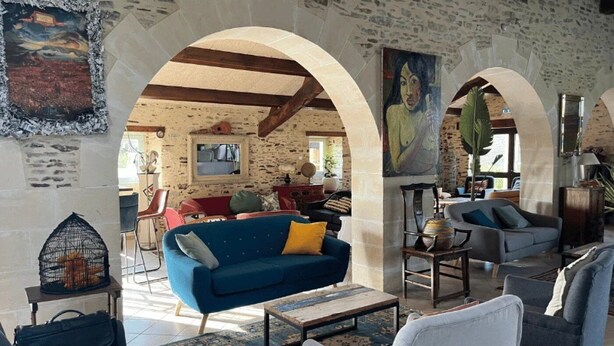 A spacious living area with a blue sofa, white armchairs, and a patterned rug. There are archways leading to another room and a large painting on the wall. - ZEcamping 3 étoiles piscine cottage TV LV 42m2 6 pers (Vouvant)