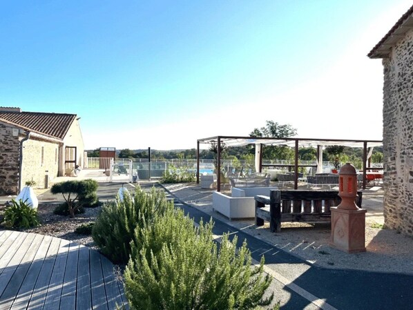 A rooftop patio with outdoor seating, a stone building, and a view of a body of water. - ZEcamping 3 étoiles piscine cottage TV LV 42m2 6 pers (Vouvant)