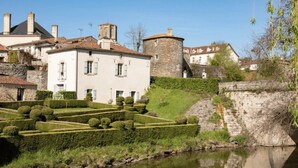 A historic building with a stone tower, surrounded by a well-maintained garden and a calm water body. - ZEcamping 3 étoiles piscine cottage TV LV 42m2 6 pers (Vouvant)