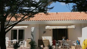 A building with a tiled roof, outdoor seating area with chairs and tables, and a small garden.