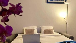 A hotel room with a bed, a laptop, a suitcase, and a glass of water on the table.