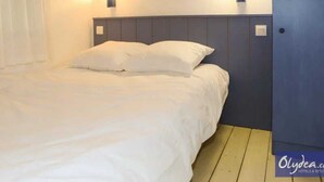 Un lit avec une literie blanche, deux lampes fixées au mur et un plancher en bois.
