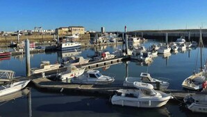 Un puerto deportivo con varios barcos amarrados, un faro y un edificio con la leyenda "SMGM" al fondo.