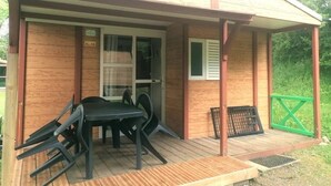 Una cabaña de madera con un porche cubierto, una mesa y sillas, y una cerca verde.