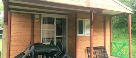 A wooden cabin with a covered porch, a table and chairs, and a green fence.