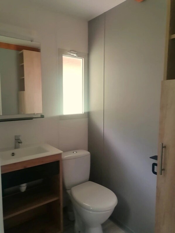 Un baño pequeño con lavamanos, espejo y retrete blancos.