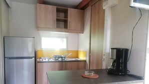 Cocina compacta con armarios de madera, refrigerador de acero inoxidable, cafetera y una pequeña isla con un bol de vidrio.