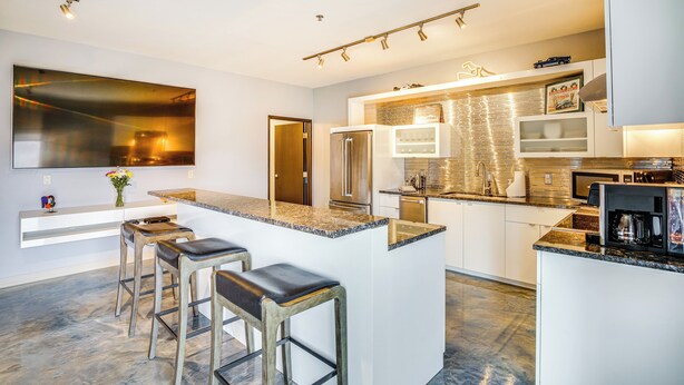 A modern kitchen with a large island, bar stools, stainless steel appliances, and a tiled backsplash. - Home Near Road America & Elkhart Lake (Elkhart Lake)