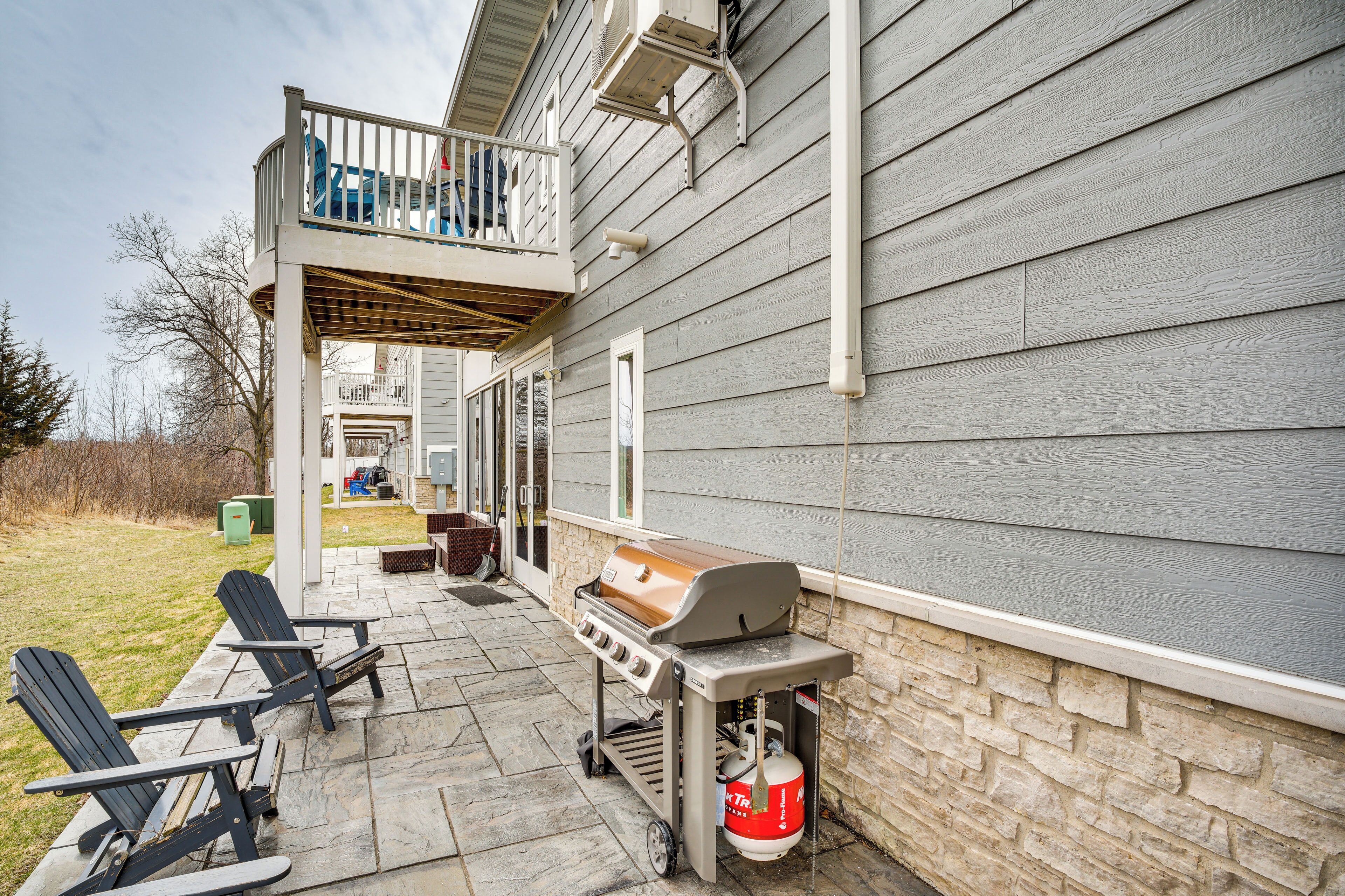 A patio with a grill, two Adirondack chairs, and a stone wall.