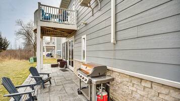 A patio with a grill, two Adirondack chairs, and a stone wall.
