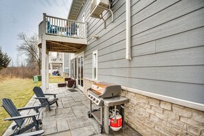 Une terrasse avec un barbecue, deux fauteuils Adirondack et un mur en pierre.