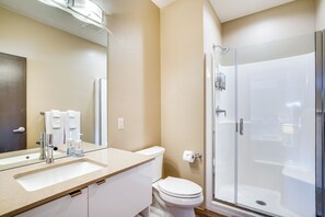 Une salle de bain équipée d’un lavabo, d’un miroir, de toilettes et d’une douche à parois de verre.