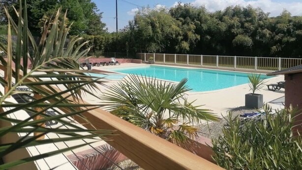 Piscina con cubierta de madera, rodeada de follaje y una valla.