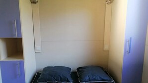 Habitación pequeña y funcional con una cama individual, dos almohadas y un armario.