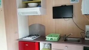Une cuisine de taille réduite, avec un réfrigérateur rouge, un évier encastré et un four à micro-ondes.